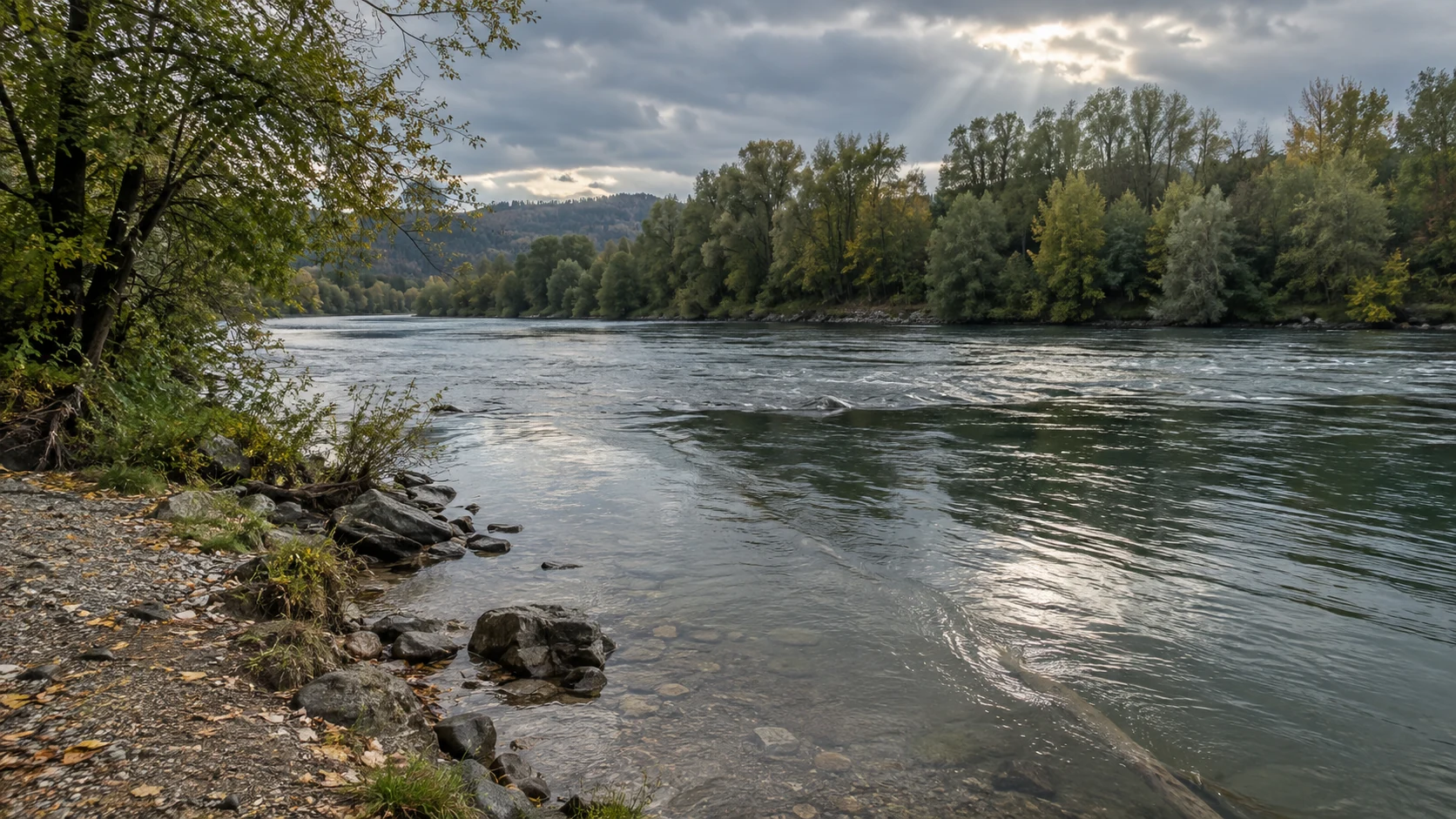 Flussufer mit Kiesweg, Strömungsübergang und aufgelockerter Wolkendecke